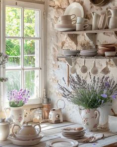 a table with plates and cups on it in front of a window filled with flowers