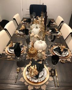 a dining room table set with black and gold place settings, white pumpkins and silverware