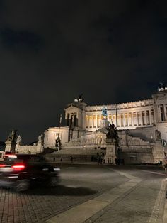 a car driving past a large building with a statue on it's side at night