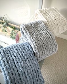 three knitted pillows sitting on top of each other in front of a window sill