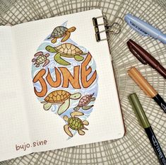 an open notebook with the word june surrounded by various stationery items including pens and markers