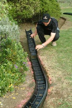 a man bending over to look at a train track in the grass near bushes and flowers