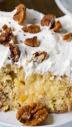 a piece of cake with white frosting and pecans on top, sitting on a plate