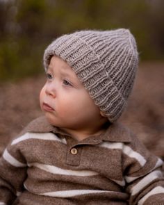 a small child wearing a striped shirt and a knitted hat sitting on the ground