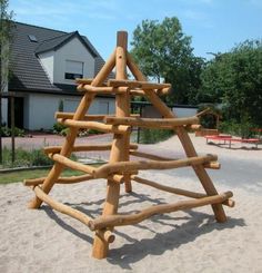 a wooden christmas tree made out of logs on the sand in front of a house