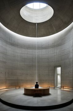 a man sitting on top of a round table in a room filled with concrete walls