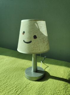 a lamp with a smiley face on it sitting on a green rug next to a wall