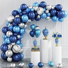 a blue and silver balloon arch with vases on the floor in front of it