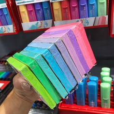 a person holding up a rainbow colored toothbrush in front of many different color bottles