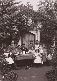 an old black and white photo of people sitting at a table in front of a house