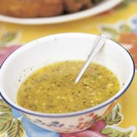 a white bowl filled with soup on top of a yellow table cloth next to meat