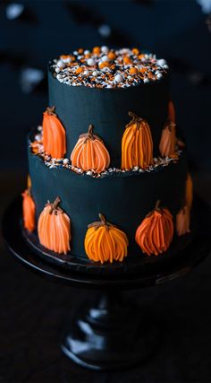 a three tiered cake decorated with pumpkins and sprinkles on a black plate