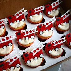 cupcakes with white frosting and red cars on them are arranged in rows