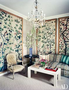 a living room filled with furniture and walls covered in floral wallpaper, along with a chandelier hanging from the ceiling