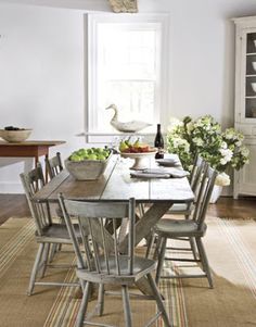 a dining room table with chairs and bowls of fruit on it in front of a window