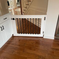 a dog gate in the middle of a kitchen with hardwood floors and white cabinets on either side