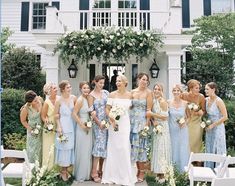 a group of women standing next to each other in front of a white house with flowers