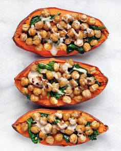 three sweet potatoes with chickpeas, spinach and cheese on them sitting on a white surface