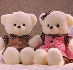 two white teddy bears sitting next to each other on top of a bed with pink sheets