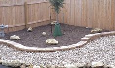 a small garden with rocks and gravel in front of a fenced area, including a tree