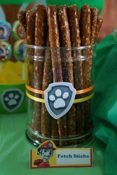 some dog treats are in a clear cup on a table with green cloth and paw stickers