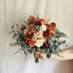 a person holding a bouquet of flowers and greenery on a white sheeted background