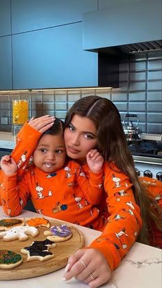 a woman and child sitting in front of a tray of cookies on a counter top