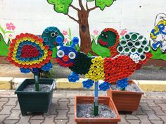 three potted plants with colorful flowers on them in front of a wall painted with children's artwork