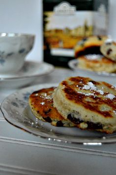 two pancakes on a plate next to a cup and saucer with powdered sugar