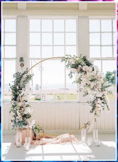 a wedding arch decorated with flowers and greenery in front of a window at the beach