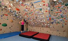 a woman standing in front of a climbing wall with red mats on the floor and two large rock walls behind her