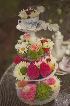 three tiered cake stand with flowers on the top and two teacups in the middle