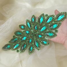 a green brooch sitting on top of a white cloth covered table next to a person's hand