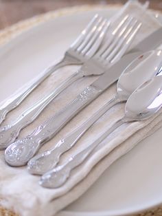 a white plate topped with silverware on top of a cloth covered place mat next to utensils