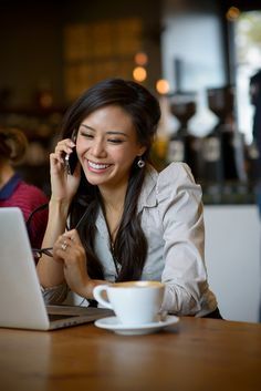 a woman sitting at a table talking on her cell phone while holding a coffee cup