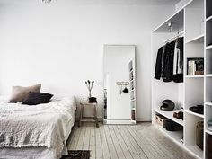 a bedroom with white walls and flooring has a bed, bookshelf, and closet