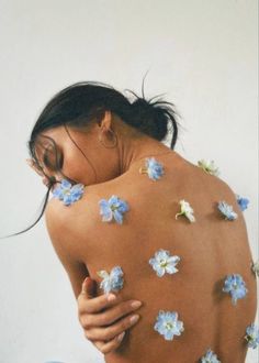 a woman with blue flowers on her back covering her face and shoulders, holding her hands to her chest