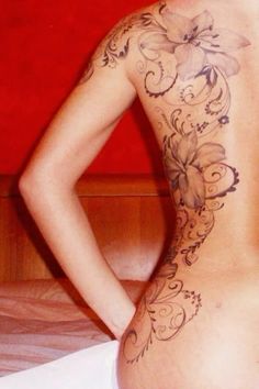 a woman with tattoos on her back standing next to a bed