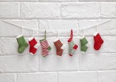 knitted christmas stockings hanging on a line against a white brick wall with red and green stocking