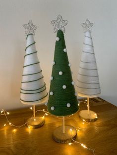 three small christmas trees sitting on top of a wooden table next to each other with lights around them