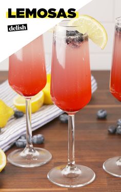 three glasses filled with lemonade sitting on top of a table next to sliced lemons and blueberries