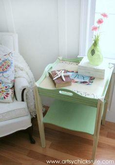 a white chair sitting next to a table with books on it and a vase filled with flowers