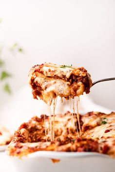 a slice of lasagna being lifted from a white casserole dish by a fork