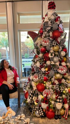 a woman sitting in front of a christmas tree with ornaments on it and other decorations