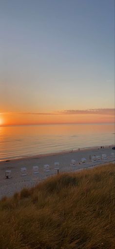 the sun is setting over the beach with chairs