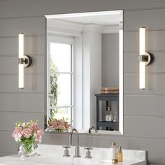 a bathroom vanity with two lights on it and a vase full of flowers in front of the mirror