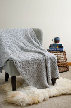 a chair with a blanket on top of it next to some books and a basket