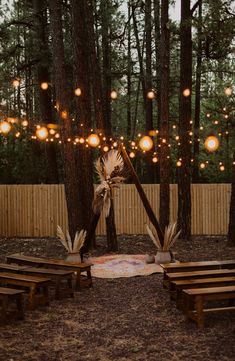 an outdoor ceremony setup with wooden benches and lights hanging from the trees in the background