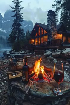 a fire pit with two glasses of wine on it in front of a log cabin