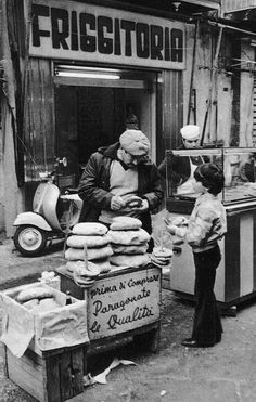 an old black and white photo of two people standing in front of a food stand